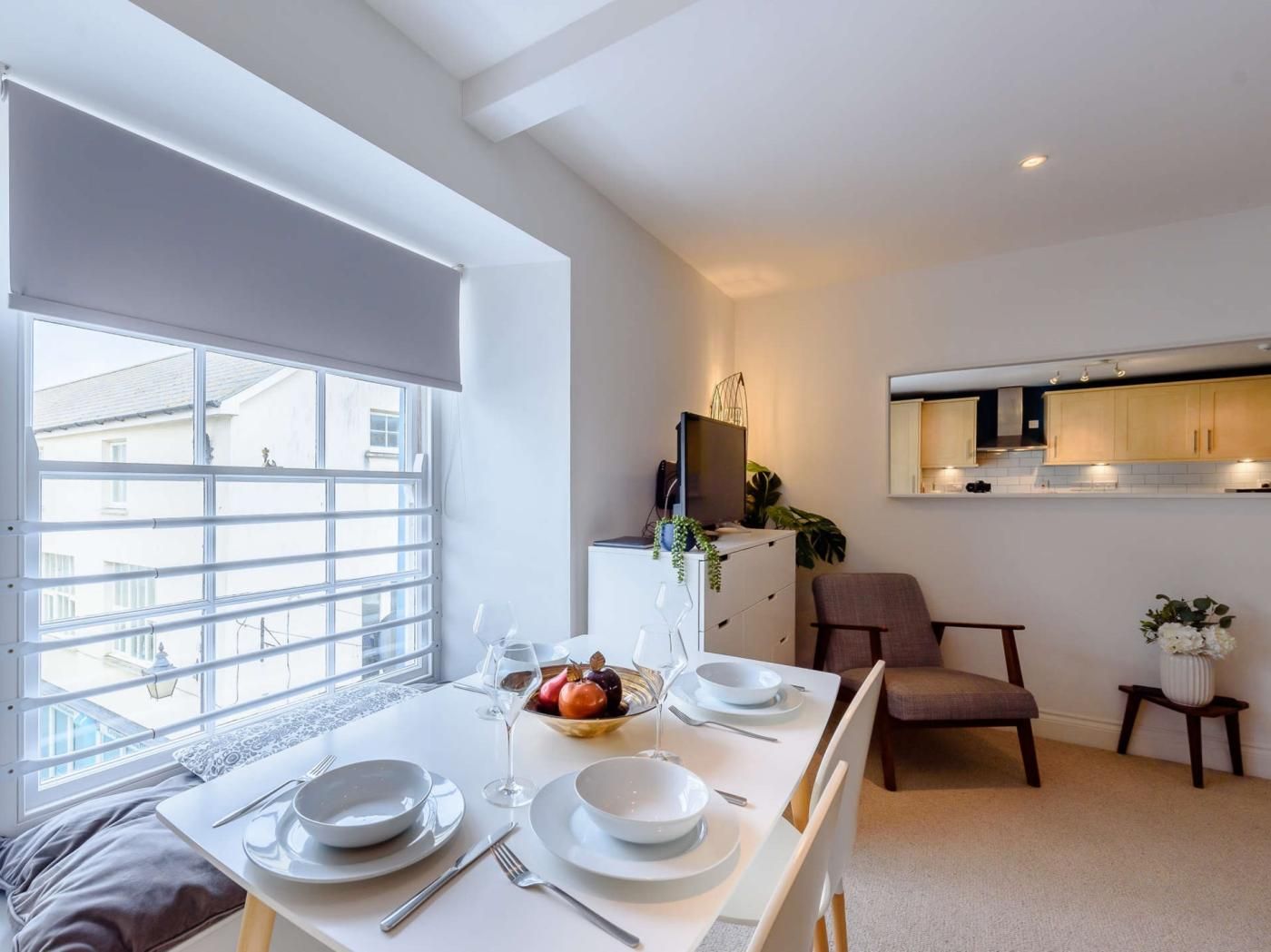 A dining area with a table set for two, a television on a cabinet, and a kitchen area with cabinets and a countertop.