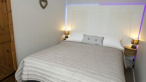 Ein Schlafzimmer mit einem Bett, zwei Nachttischen mit Lampen, einer herzförmigen Dekoration an der Wand und einer Holztür.