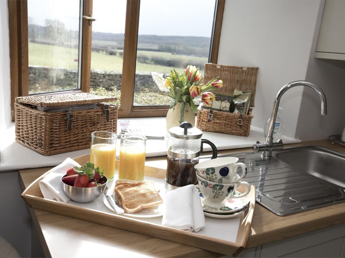 A breakfast tray with toast, strawberries, juice, coffee, and a teapot on a kitchen counter.
