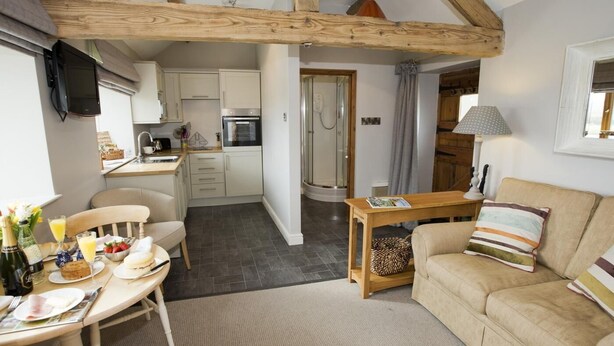 Ein gemütliches Interieur mit Essbereich, Küche und Wohnzimmer, das freiliegende Holzbalken und einen Kamin zeigt.