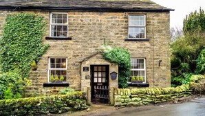 A stone building with a central entrance, windows on the upper floor, and a stone wall with greenery. - 2 Bed in Harrogate (oc-g0017) (Lofthouse)