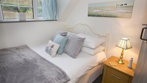 Et soveværelse med seng, et sengebord med lampe, et vindue med gardiner og et billede på væggen.