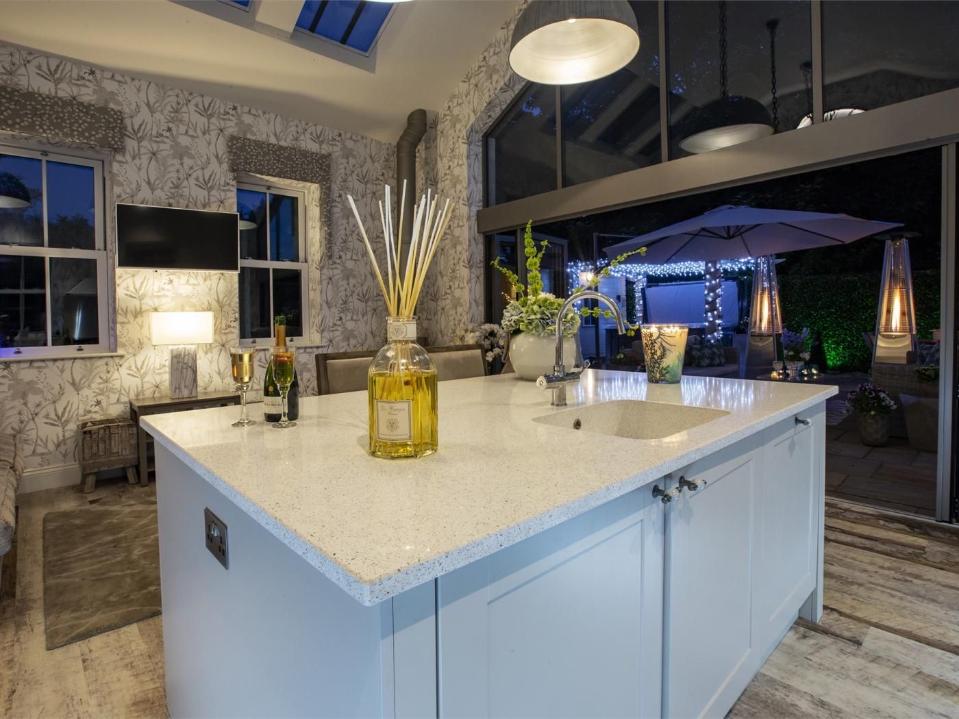 A modern kitchen with a large island, a built-in sink, and a window overlooking a garden.