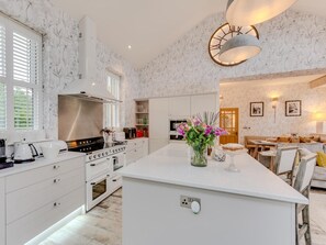 A modern kitchen with white cabinetry, a central island, and a dining area with a wooden table and chairs. - 3 Bed in Leyburn (oc-g0133) (Preston-under-Scar)