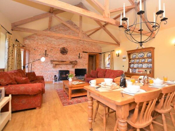 A cozy living room with a fireplace, a dining area with a table set for breakfast, and a brick wall with a clock. - 2 Bed in Market Rasen (oc-73853) (East Barkwith)