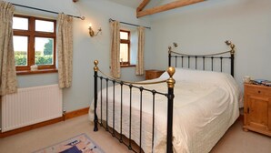 Ein Schlafzimmer mit einem Bett, Holzbalken, einer Heizung und einem Fenster mit Vorhängen.