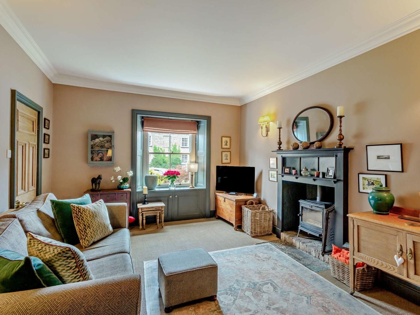 A cozy living room with a sofa, ottoman, fireplace, television, and a window with a view.
