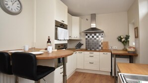 Een moderne keuken met witte kasten, een roestvrijstalen afzuigkap, een ronde tafel met een zwarte stoel, en een wandklok.