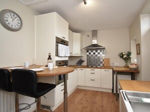 A modern kitchen with white cabinets, a stainless steel range hood, a round table with a black chair, and a wall clock. - 2 Bed in Bishop Auckland (oc-82620) (Cockfield)