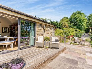 A modern outdoor patio with wicker furniture, a stone wall, and a glass door leading to a dining area. - 2 Bed in Hampsthwaite (oc-g0156) (Clint)