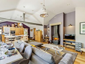 A modern living room with a fireplace, a dining area, and a kitchen with wooden cabinets. - 2 Bed in Hampsthwaite (oc-g0156) (Clint)