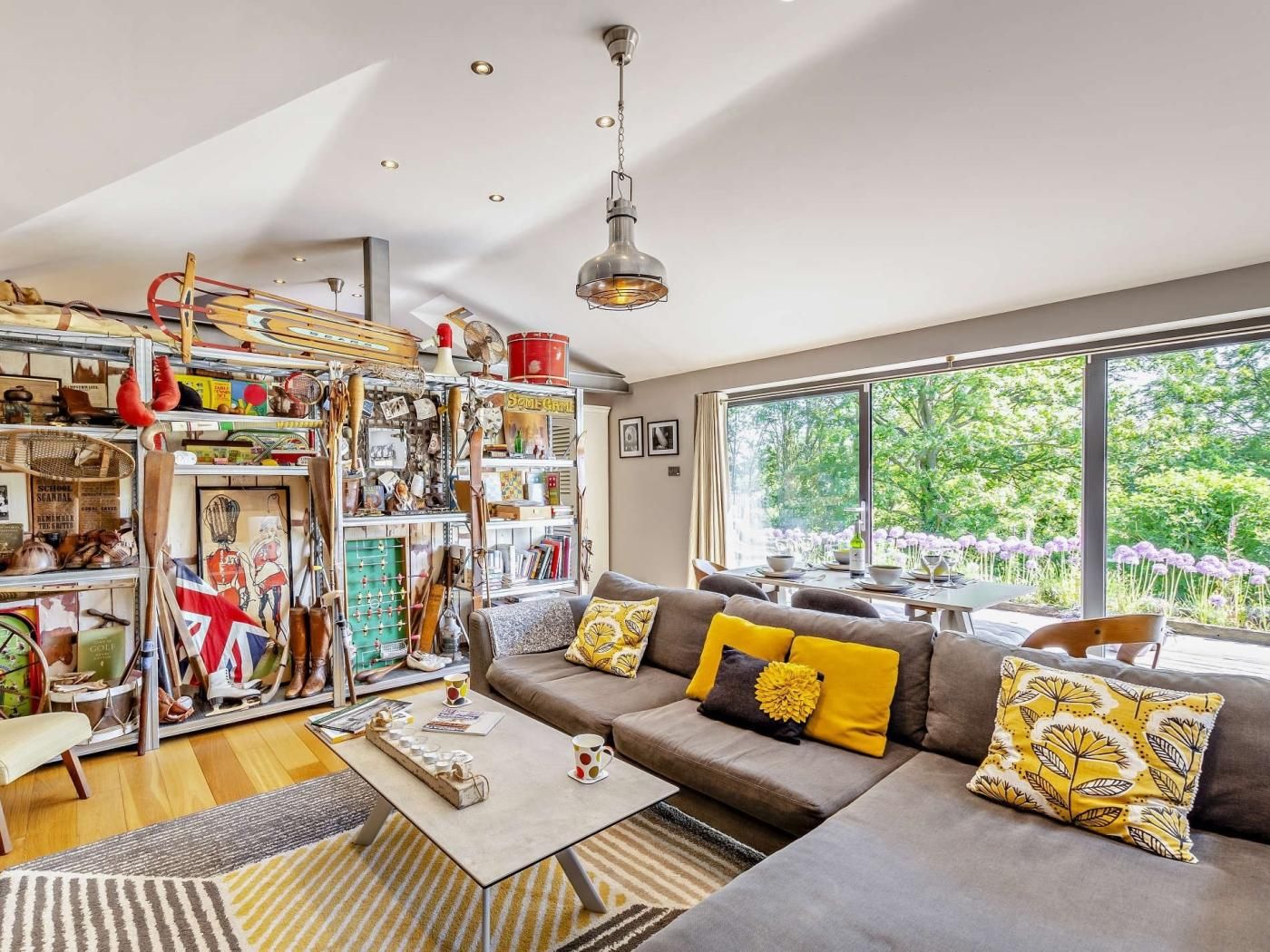A modern living room with a sectional sofa, a coffee table, and a bookshelf filled with various items.