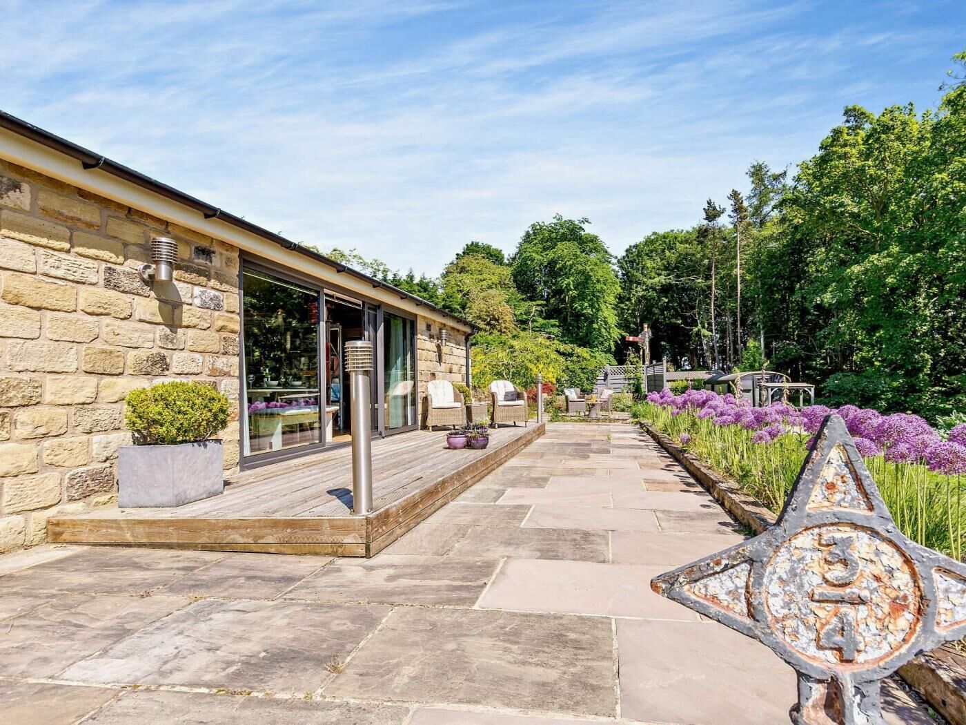 Ein Steinhaus mit Terrasse, Außenbestuhlung und einem Garten mit violetten Blumen.