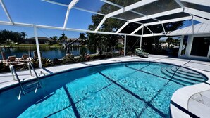 En swimmingpool med klart, blåt vand, omgivet af en hvid bygning, samt udsigt over det omkringliggende landskab.
