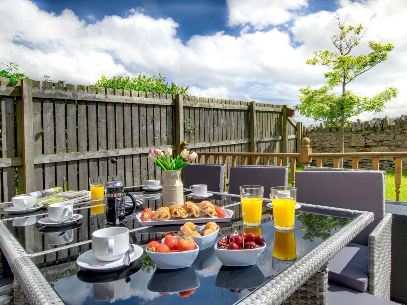 An outdoor dining area with a table set for breakfast, including croissants, fruit, and juice.