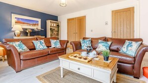 Ein Wohnzimmer mit zwei braunen Ledersofas, einem weißen Couchtisch, einem Holzschrank, einem Bild an der Wand und zwei Holztüren.