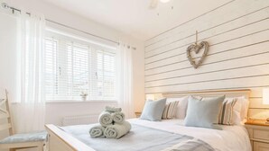 Ein Schlafzimmer mit einem Bett, einem Nachttisch, einem Stuhl, einem Fenster mit Vorhängen und einer herzförmigen Dekoration an der Wand.