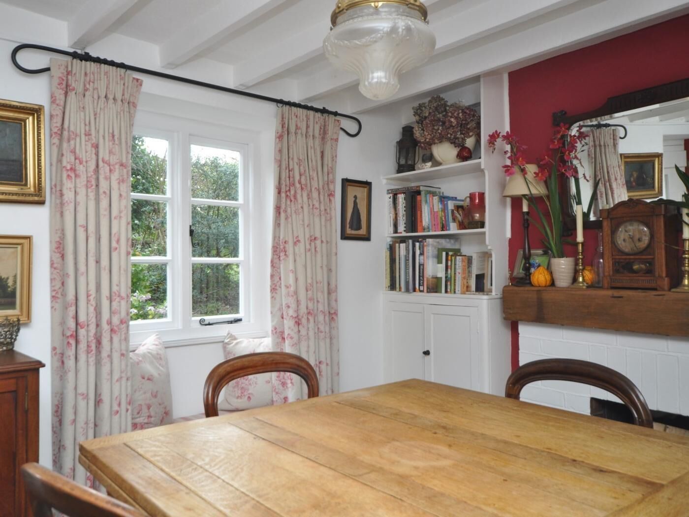 Un coin repas avec une table en bois, des chaises, une bibliothèque et une fenêtre avec des rideaux.