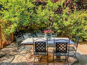 Een terras buiten, met een tafel en stoelen, omringd door weelderige beplanting.
