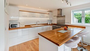 A modern kitchen with white cabinets, a wooden countertop, a stainless steel range hood, and a window with a view of greenery. - 3 Bed in Woolacombe (oc-74255) (Woolacombe)