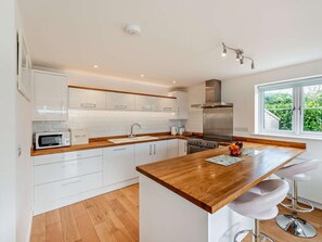 A modern kitchen with white cabinets, a wooden countertop, a stainless steel range hood, and a window with a view of greenery. - 3 Bed in Woolacombe (oc-74255) (Woolacombe)