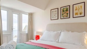 A hotel room with a bed, a window with curtains, and three framed botanical prints on the wall. - 4 Bed in Bridport (oc-dc083) (West Bay)