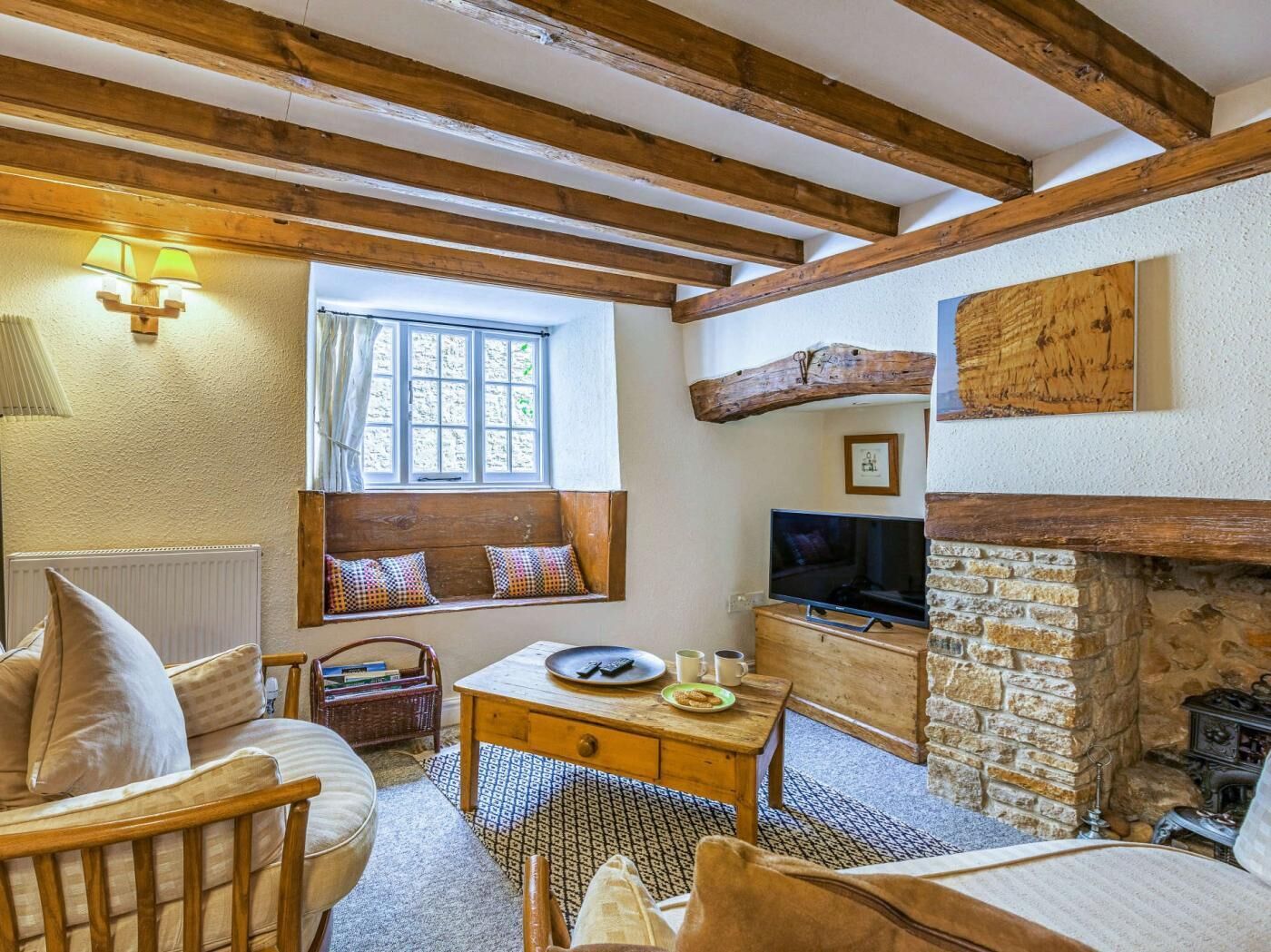 A cozy room with exposed wooden beams, a stone fireplace, a television, and a window with a view.