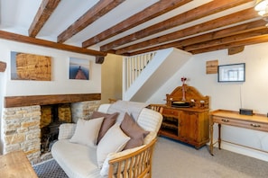 A cozy room with a stone fireplace, wooden beams, a sofa, a desk, and a staircase. - 2 Bed in Bridport (oc-dc148) (Burton Bradstock)