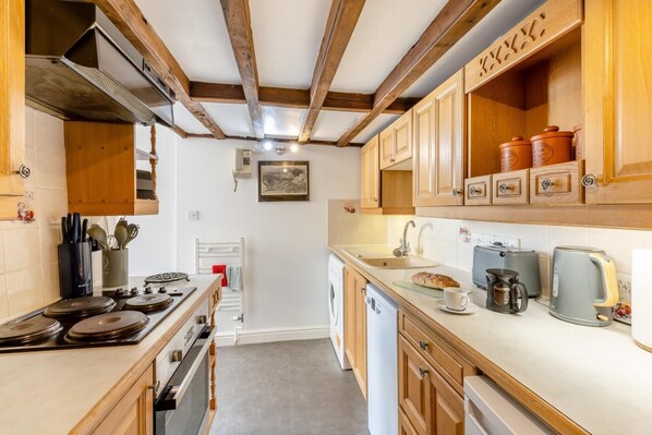 A kitchen with wooden cabinets, a stove, a sink, and a toaster. - 2 Bed in Bridport (oc-dc148) (Burton Bradstock)