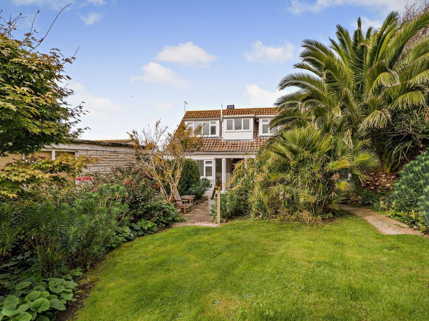 Une maison à deux étages avec un jardin, un mur en pierre et un palmier.