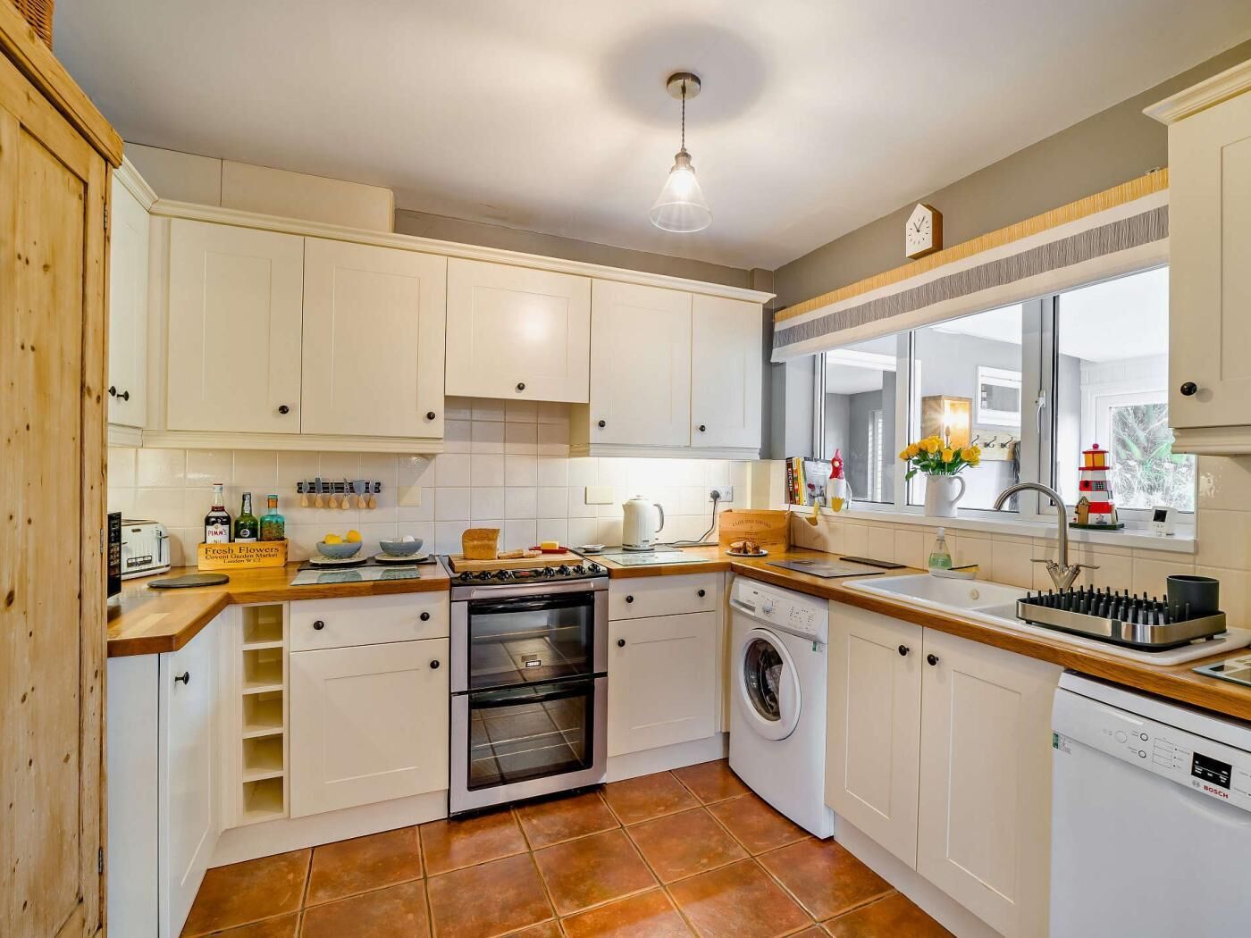 A compact kitchen with white cabinets, a built-in oven, a washing machine, and a window with a view.