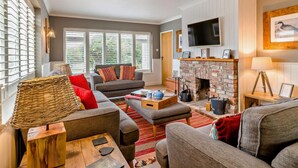 Een woonkamer met een open haard, een televisie en een groot raam met zonwering.