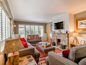 A living room with a fireplace, a television, and a large window with blinds. - 4 Bed in Dorchester (oc-dc149) (West Bexington)
