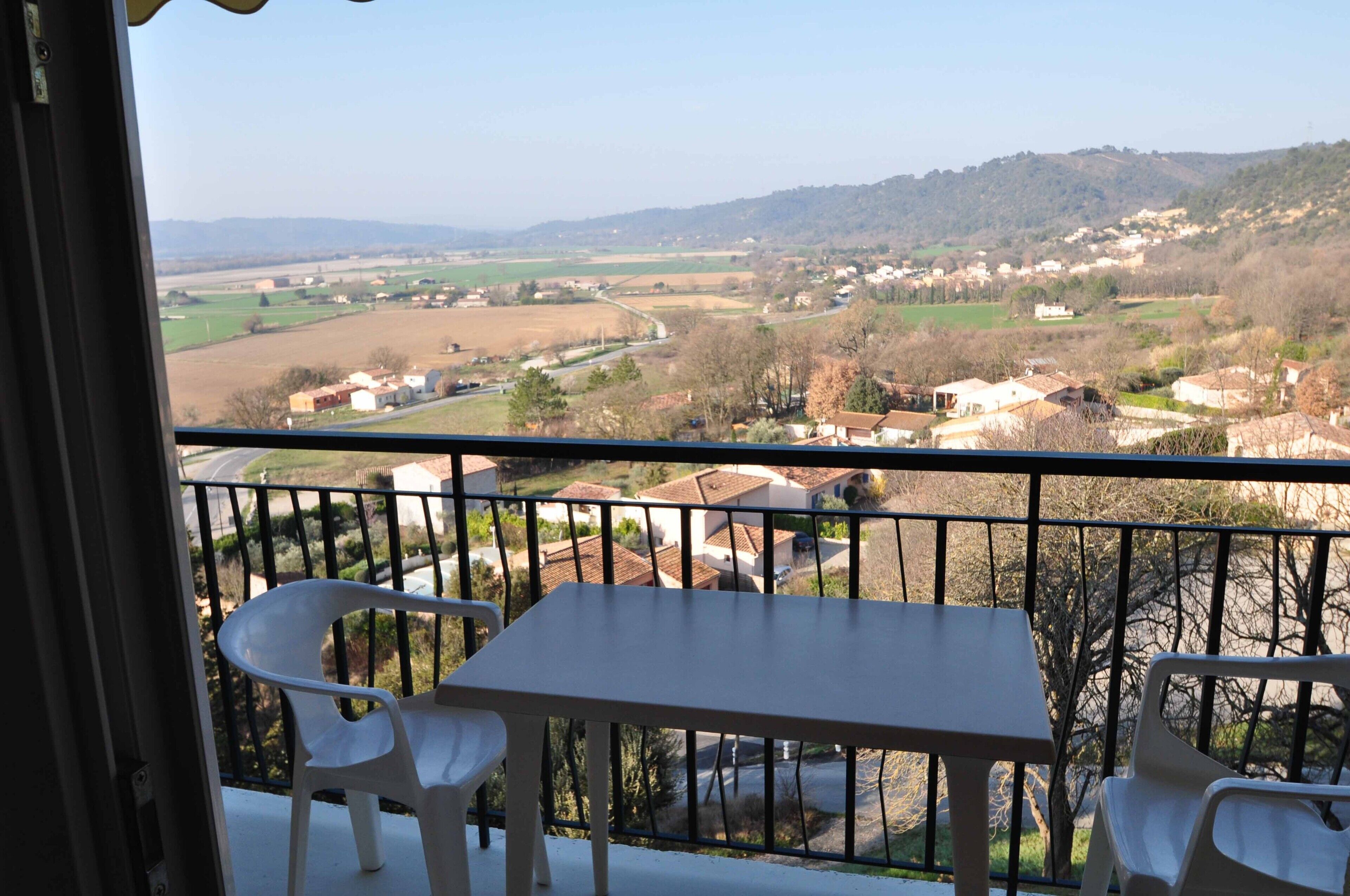 Un balcon avec une table et des chaises, offrant une vue sur un paysage rural avec des champs et des maisons.