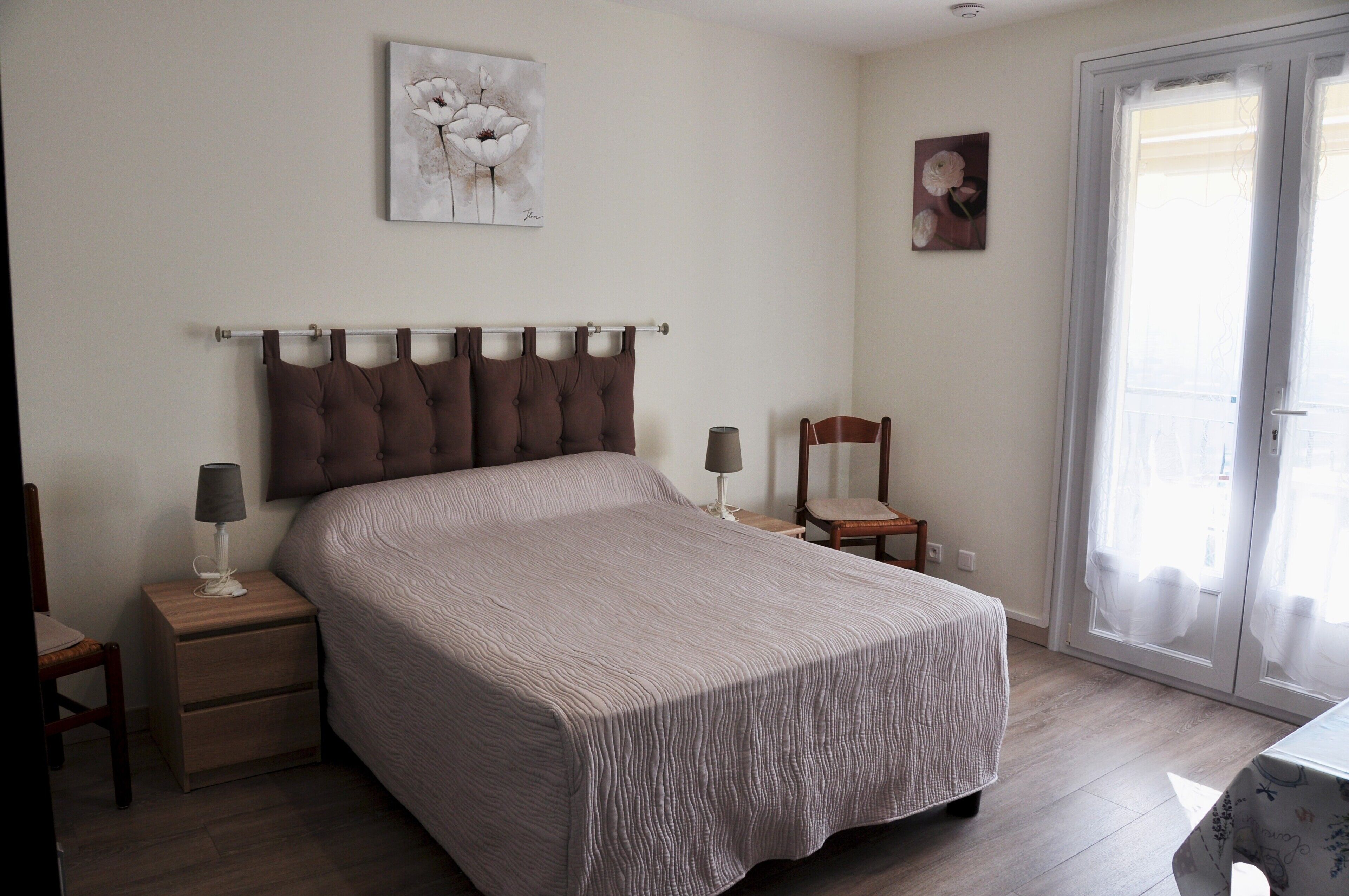 A bedroom with a bed, two bedside tables, a nightstand, a chair, and a door with a view.