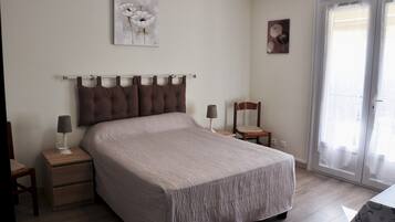 A bedroom with a bed, two bedside tables, a nightstand, a chair, and a door with a view.
