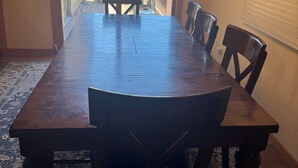 Ein Esszimmer mit einem großen Holztisch und Stühlen, einem gemusterten Teppich und Blick durch eine Glastür auf einen Außenbereich mit einem Grill.