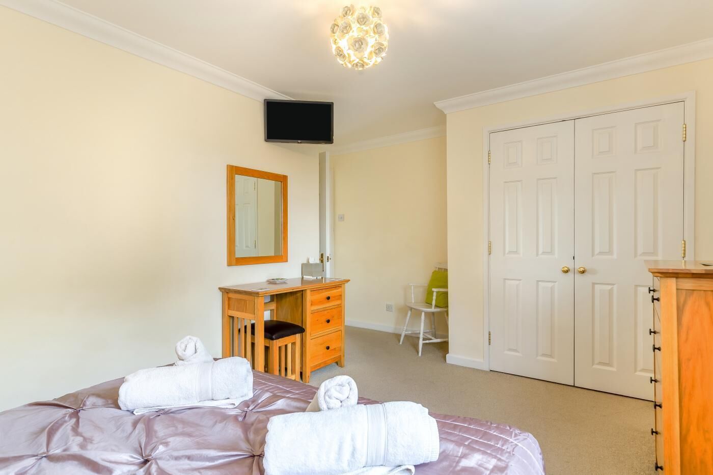 Une chambre à coucher comprenant un lit, une commode en bois, un bureau, une chaise, un téléviseur et une armoire.