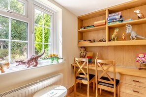 Ein Kinderzimmer mit Fenster, Heizkörper, Schreibtisch mit Büchern und Spielzeug sowie einem Stuhl.