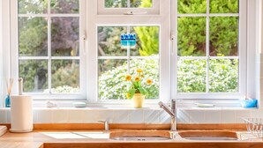 A kitchen with a double sink, a window with a view of greenery, and a potted plant on the windowsill. - 4 Bed in Dorchester (oc-dc133) (Winfrith Newburgh)