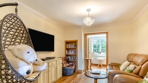 A living room with a hanging chair, a sofa, a coffee table, a bookshelf, and a television. - 4 Bed in Dorchester (oc-dc133) (Winfrith Newburgh)