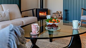 Una sala de estar acogedora con un sofá, una mesa de centro de vidrio con un cuenco de fruta, una taza y una chimenea.