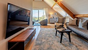 Un dormitorio estilo loft moderno con techo inclinado, televisor grande, sofá y comedor.