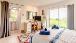 A bedroom with a bed, a desk, a television, a mirror, a window, and a bathroom. - 3 Bed in Swanage (oc-dc140) (Worth Matravers)