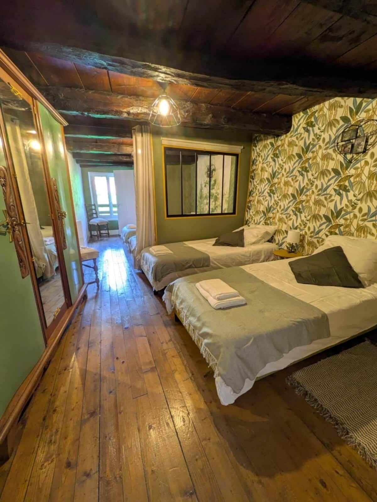 Una habitación con dos camas, piso de madera, un espejo y una ventana con persianas.