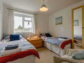 A bedroom with two beds, a nightstand, a wicker chair, and a window with curtains. - 3 Bed in Bridport (oc-dc117) (West Bay)