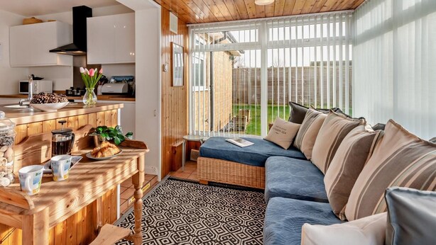 Eine moderne Küche mit Holzelementen, ein Essbereich mit einem blauen Sofa und Blick auf einen Garten durch große Fenster.