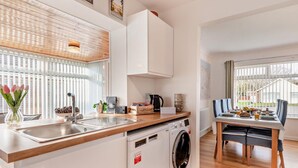 Eine kompakte Küche mit Waschmaschine, ein Essbereich mit Tisch und Stühlen sowie ein Fenster mit Jalousien.