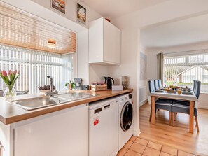 Eine kompakte Küche mit Waschmaschine, ein Essbereich mit Tisch und Stühlen sowie ein Fenster mit Jalousien.