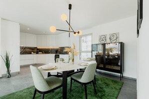 Un comedor moderno con una mesa blanca, sillas verdes, una lámpara de araña negra y una alfombra verde.